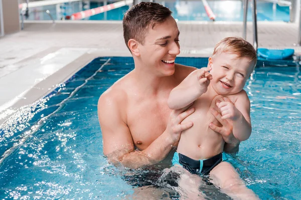 Happy trainer holding in arms toddler kid in swimming pool — Stock Photo