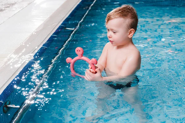 Cute toddler kid playing with rubber toy in swimming pool — Stock Photo