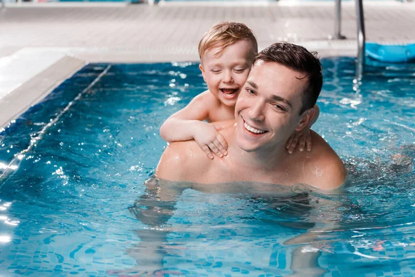 Niño feliz y entrenador de natación sonriendo en la piscina - foto de stock