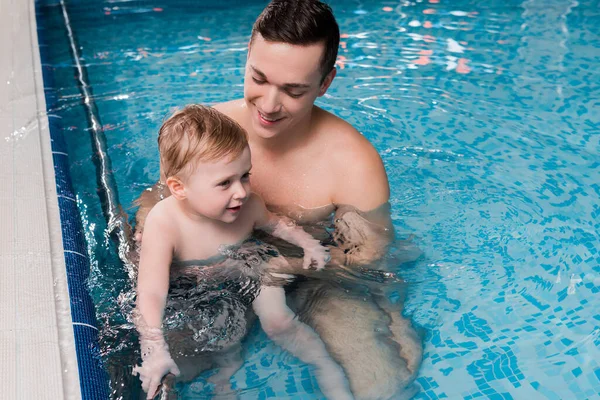 Entrenador de natación feliz enseñando niño pequeño en la piscina - foto de stock