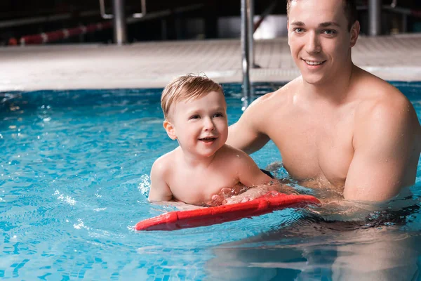 Allegro allenatore di nuoto che insegna allegro bambino con flutter board in piscina — Foto stock