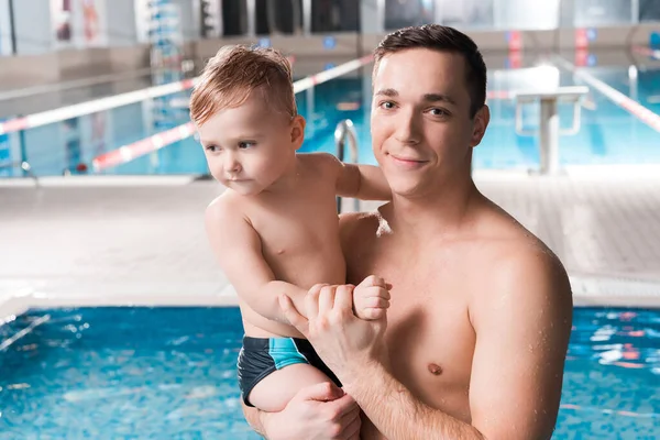 Happy swim trainer holding in arms toddler kid near swimming pool — Stock Photo