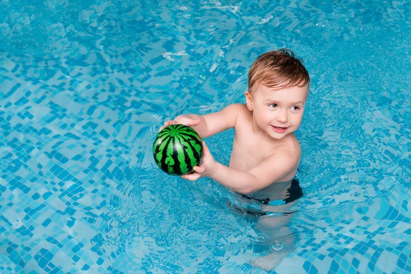 Cute toddler boy swimming with inflatable ball in swimming pool — Stock Photo