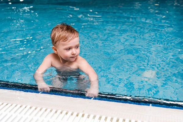 Cute toddler boy in swimming pool with blue water — Stock Photo
