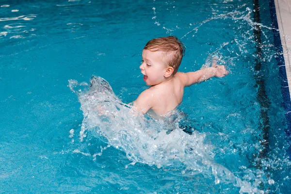 Возбужденный мальчик брызгает водой в бассейне — стоковое фото
