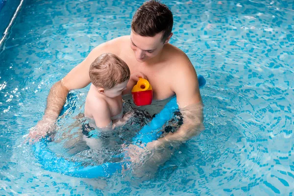 Beau entraîneur de natation avec nouilles de piscine près de tout-petit enfant — Photo de stock