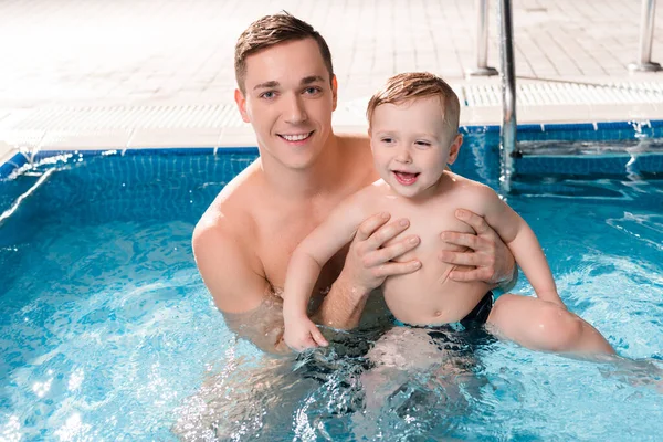 Guapo entrenador de natación nadando con niño alegre en la piscina - foto de stock