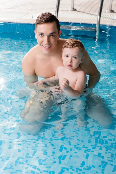 Heureux entraîneur de natation nager avec tout-petit enfant dans la piscine — Photo de stock