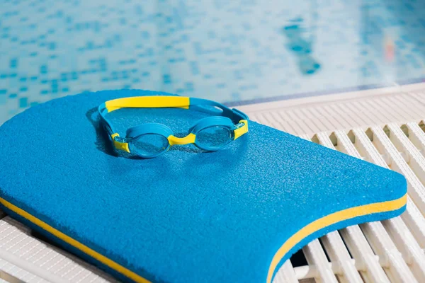 Goggles on flutter board near swimming pool with blue water — Stock Photo