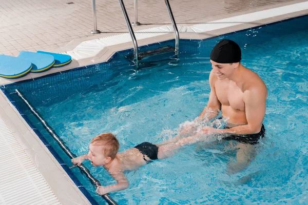 Smiling swim coach in swimming cap training toddler kid in swimming pool — Stock Photo