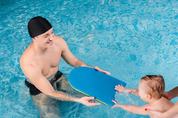 Vista aérea de la madre tocando lindo niño nadando cerca de instructor de natación - foto de stock