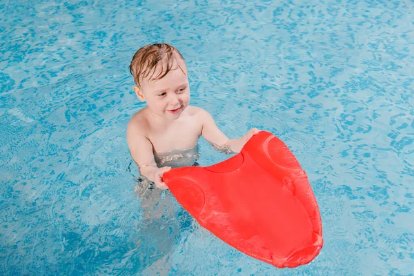 Menino criança feliz nadando com prancha de vibração na piscina — Fotografia de Stock