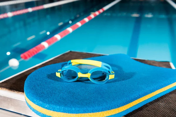 Goggles on blue flutter board near swimming pool — Stock Photo