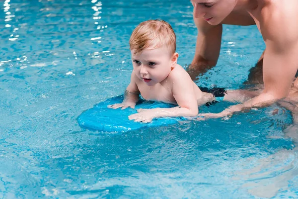 Niño pequeño nadando con tabla de aleteo cerca de entrenador de natación - foto de stock