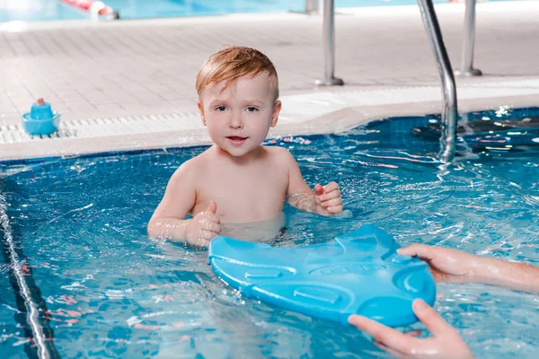 Swim trainer holding flutter board near cute toddler boy in swimming pool — Stock Photo