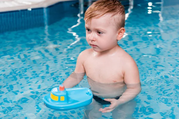 Niedlicher Kleinkind Junge spielt mit Spielzeugschiff im Schwimmbad — Stockfoto