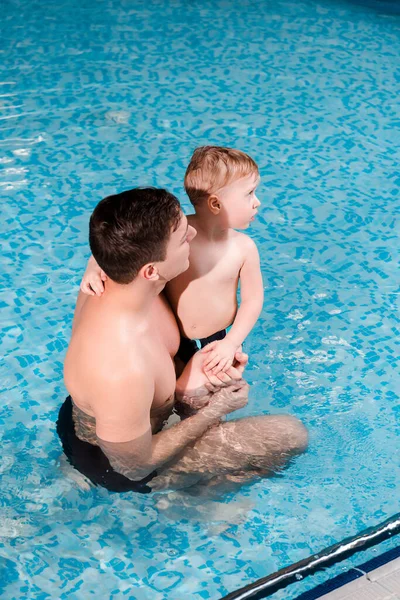 Entrenador de natación celebración en brazos lindo niño en la piscina - foto de stock