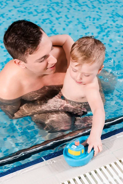Overhead view of swim coach looking at toddler boy touching toy ship — Stock Photo