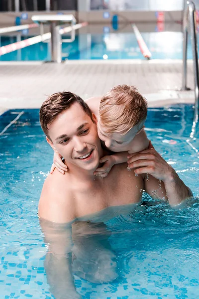 Милый мальчик обнимает счастливого тренера по плаванию в бассейне — стоковое фото