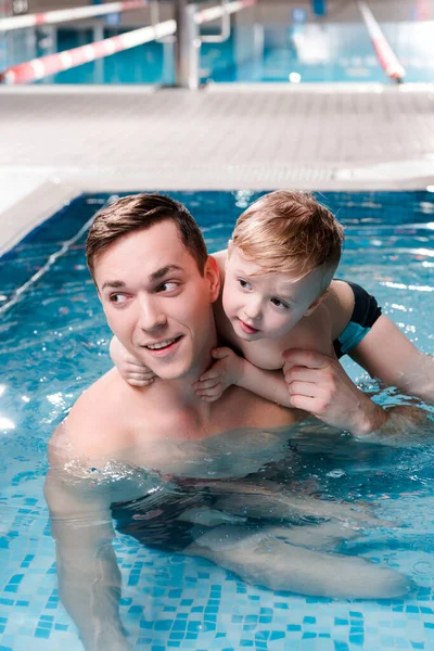 Милый мальчик обнимает красивого тренера по плаванию в бассейне — стоковое фото