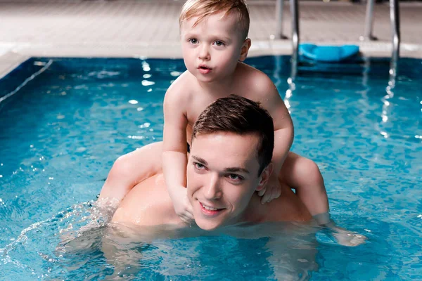 Handsome swim coach holding cute toddler kid on shoulders in swimming pool — Stock Photo