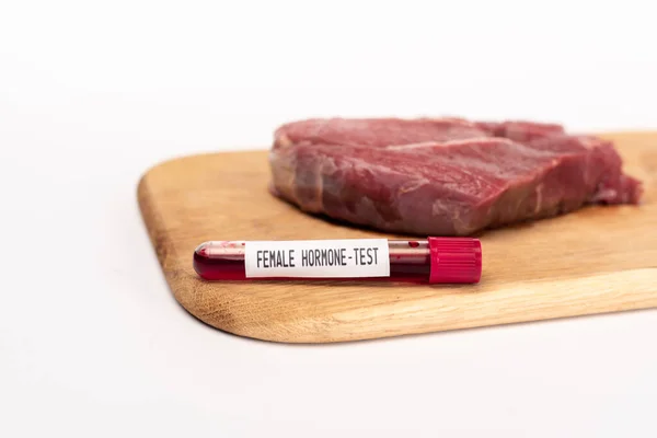 Foco seletivo do tubo de teste com teste de hormônio feminino em tábua de corte com carne crua isolada em branco — Fotografia de Stock