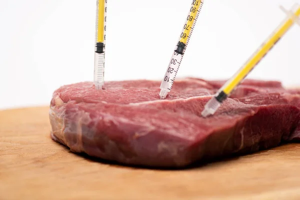 Foco seletivo de seringas em carne crua em tábua de corte isolada em branco — Fotografia de Stock
