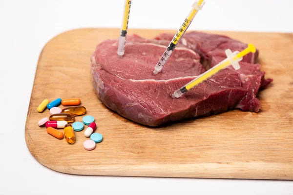 Seringas em carne crua e pílulas hormonais na tábua de corte isolada em branco — Fotografia de Stock