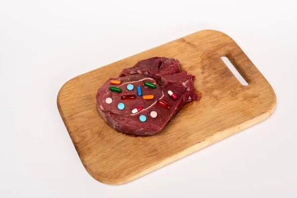 Vista ad alto angolo di pillole ormonali su pezzo di carne cruda sul tagliere isolato su bianco — Foto stock