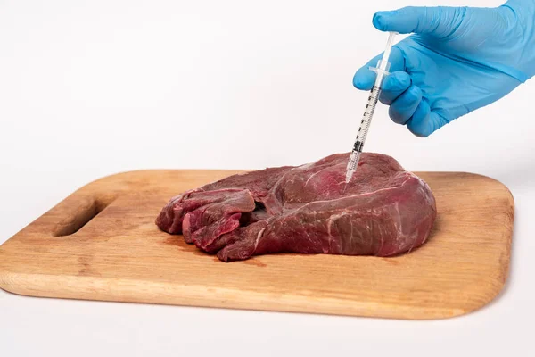 Vista ritagliata del medico che fa l'iniezione ormonale nella carne cruda sul tagliere su sfondo bianco — Foto stock