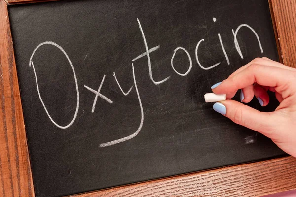 Cropped view of woman holding piece of chalk near blackboard with oxytocin lettering — Stock Photo