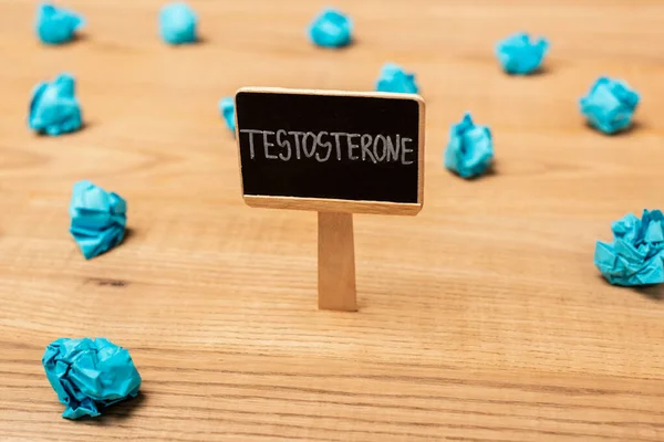 Close up view of nameplate with testosterone lettering near crumpled paper on wooden surface — Stock Photo