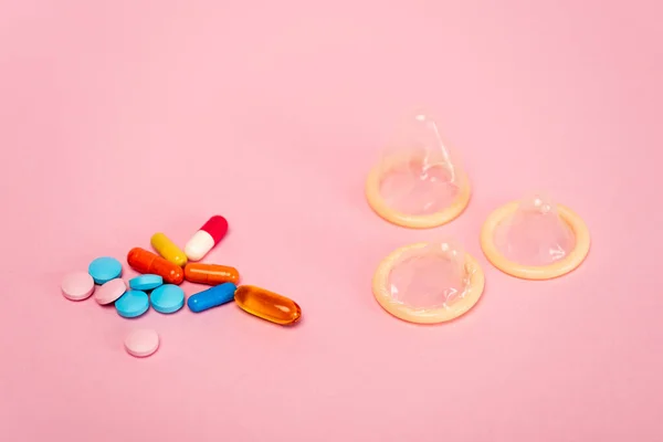 Vista de cerca de condones y píldoras anticonceptivas sobre fondo rosa - foto de stock