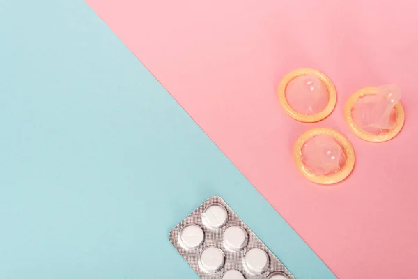 Вид зверху блістер з таблетками контролю народжуваності та презервативами на рожево-блакитній поверхні — стокове фото
