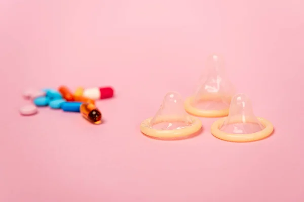 Selective focus of condoms and birth control pills on pink background — Stock Photo