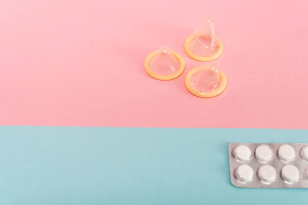 Vue en angle élevé des préservatifs et des pilules contraceptives sur la surface rose et bleue — Photo de stock