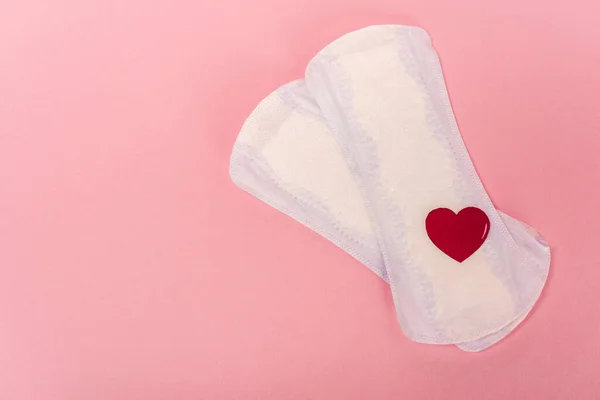 Top view of feminine pads with paper heart on pink background — Stock Photo