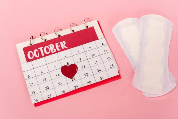 Vista de alto ângulo do calendário com coração de papel perto de almofadas femininas no fundo rosa — Fotografia de Stock