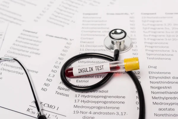 Vue rapprochée du stéthoscope et du tube à essai avec inscription d'insuline sur les listes contenant des hormones — Photo de stock