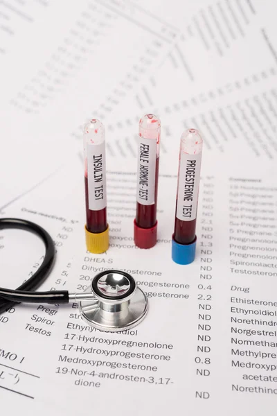 Close up view of stethoscope and test tubes with hormone and insulin tests on lists with hormones — Stock Photo