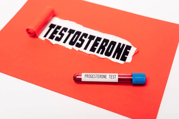 Nahaufnahme des Reagenzglases mit Progesteron-Blutprobe in der Nähe von rotem Papier mit Testosteron-Schriftzug isoliert auf weißem Papier — Stockfoto