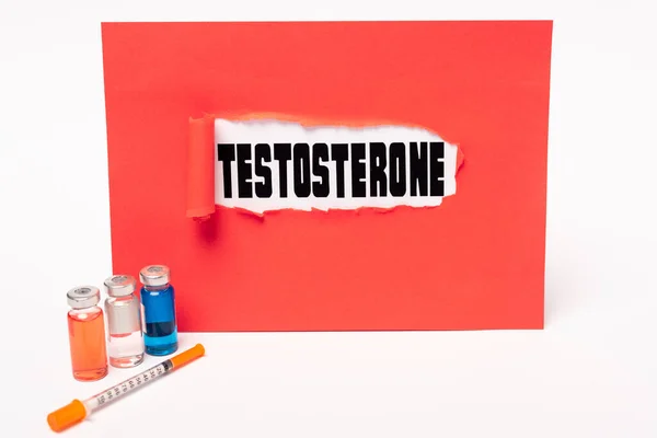 Надпись на тестостероне в красной бумаге, шприце и банках гормональных препаратов на белом фоне — стоковое фото