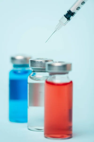 Selective focus of syringe near jars with colored hormonal drugs on blue surface — Stock Photo