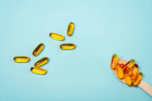 High angle view of wooden spoon and pills with fish oil on blue surface — Stock Photo