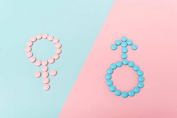 Высокий угол обзора мужских и женских признаков от гормональных таблеток на голубой и розовой поверхности — стоковое фото