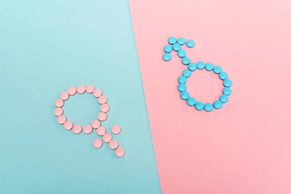 Vista ad alto angolo di segni femminili e maschili da pillole ormonali su sfondo blu e rosa — Foto stock