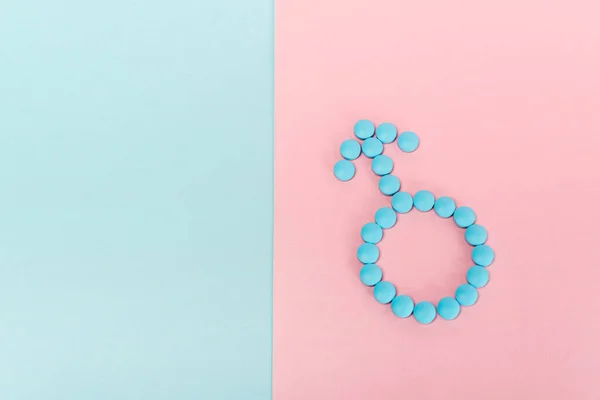 Vista superior del signo masculino de píldoras hormonales en la superficie azul y rosa - foto de stock