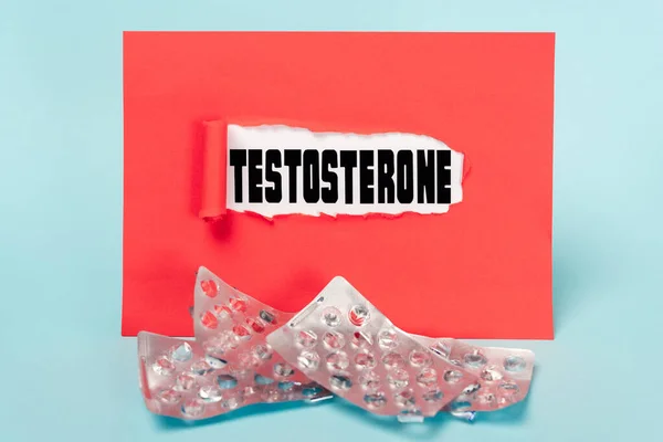 Papel con letras de testosterona y ampollas vacías de pastillas sobre fondo azul - foto de stock
