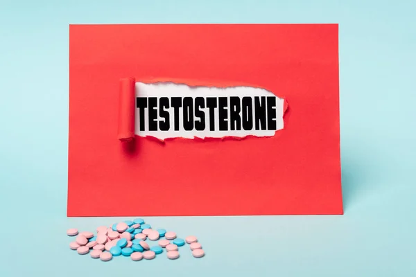 Hormonal pills and testosterone lettering in hole of red paper on blue background — Stock Photo