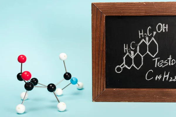 Hormone construction near blackboard with formula of testosterone on blue background — Stock Photo